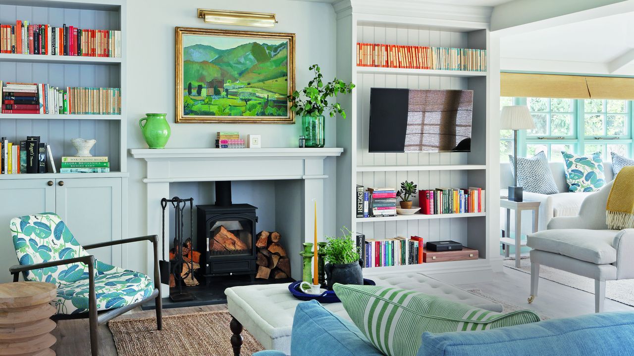 colorful living room with woodburner, paneled bookcases, patterned chair, blue sofa, white chair, stool and colorful patterned cushions