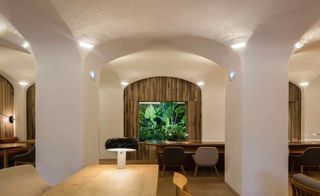 A large sitting are with two longs tables, chairs, wall feature made of plants and arched ceilings.