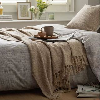 cosy bedroom with throw blanket and tray with mug and pile of magazines