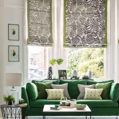 Neutral living room with a deep forest green sofa and patterned Roman blinds