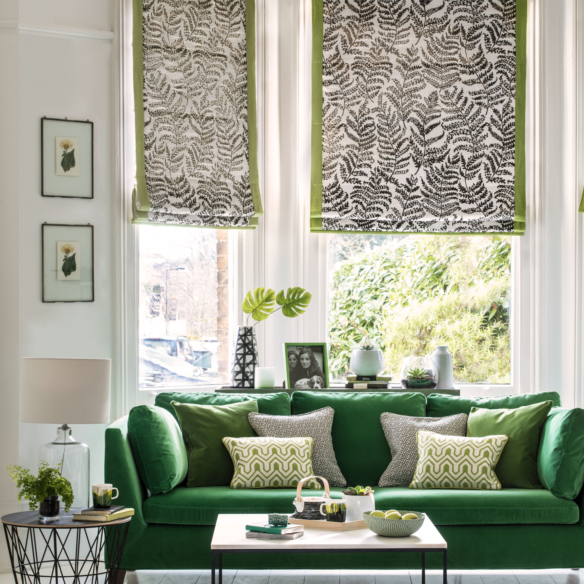 Neutral living room with a deep forest green sofa and patterned Roman blinds