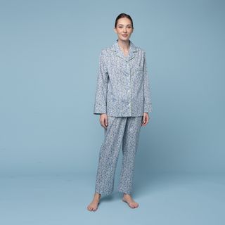 A floral pajama set in tones of blue is worn by a model against a light blue background.