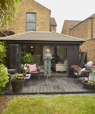 A woman standing on a b;lack decking in front of a kitchen extension with bifold doors