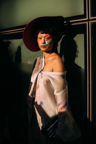 a show attendee at Milan Fashion week with colorful makeup and a feather hat