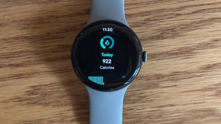 The Google Pixel Watch 3 sitting on a desk, showing a daily calorie count widget.