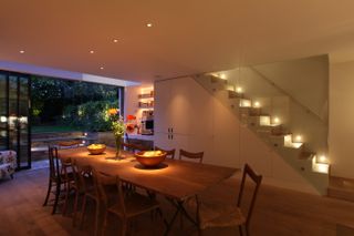 Basement kitchen with dining table and chairs and staircase with lighting on and view to garden