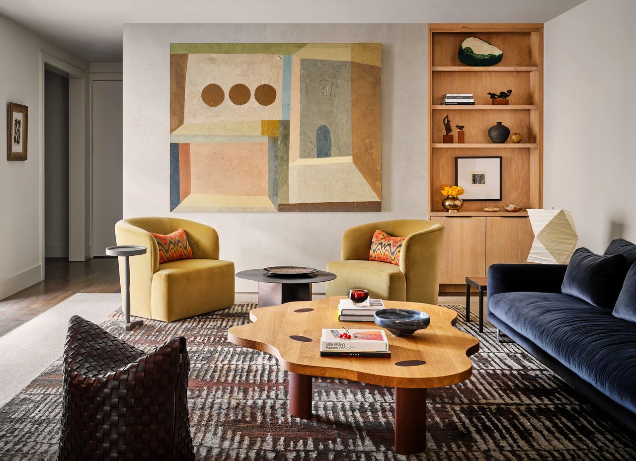 modern living room with gray velvet sofa, artwork, yellow velvet armchair, chrome side table, timber wiggly coffee table, accent lighting, patterned rug and built-in bookshelves