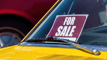 A bright yellow car has a "for sale" sign in the front window.