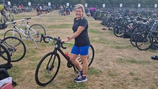 Sarah Finley holding bike in triathlon transition zone smiling at the camera