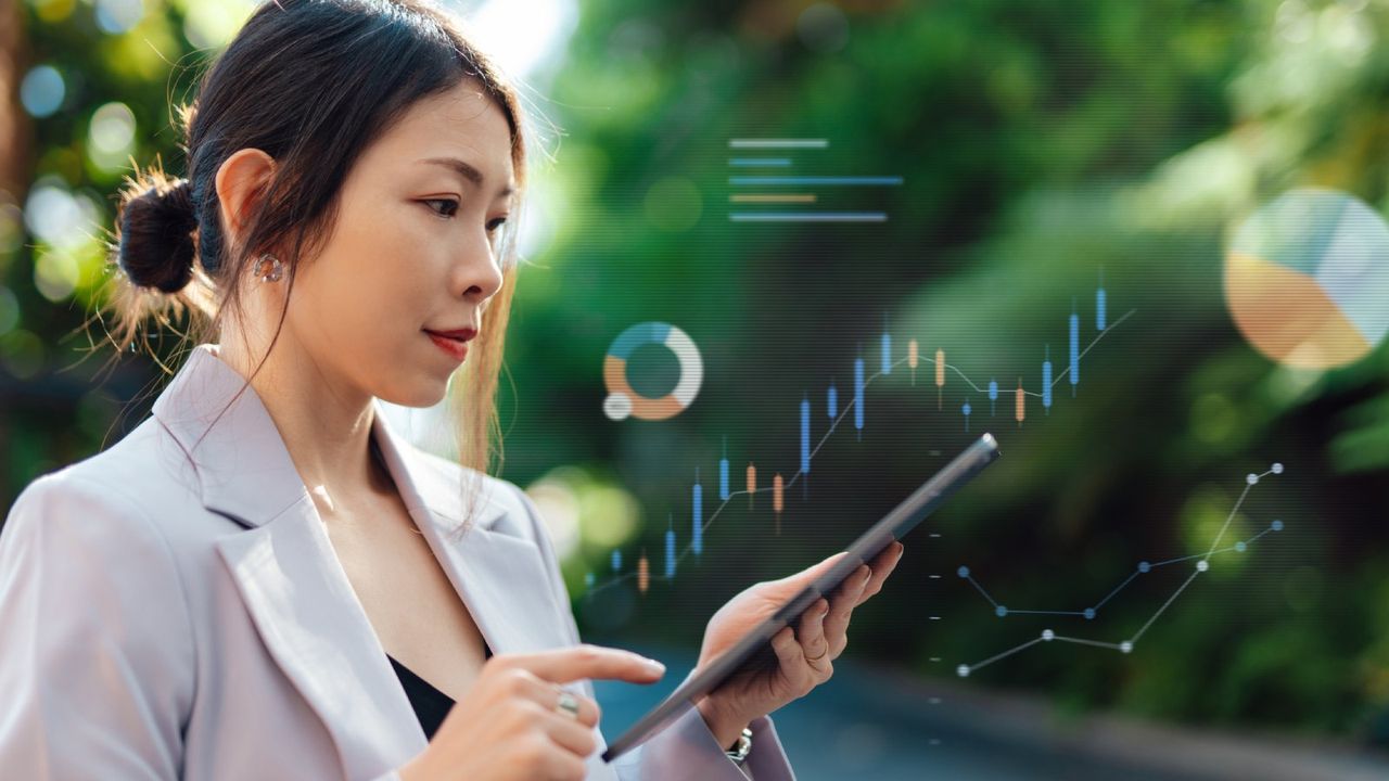 A woman holds a tablet in front of trees. She is surrounded by technological graphics