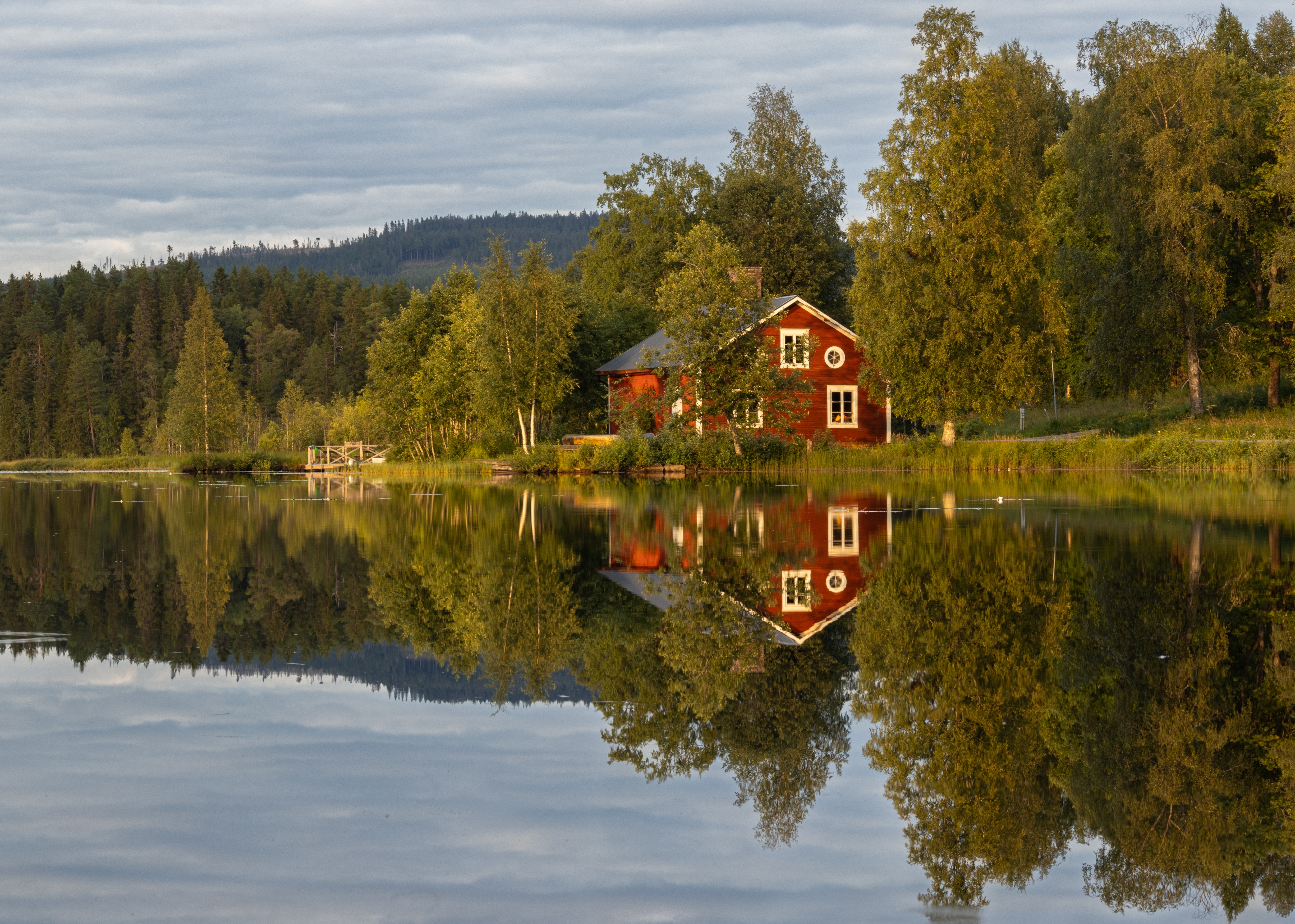 Swedish stuga by a calm lake on a cloudy summer day