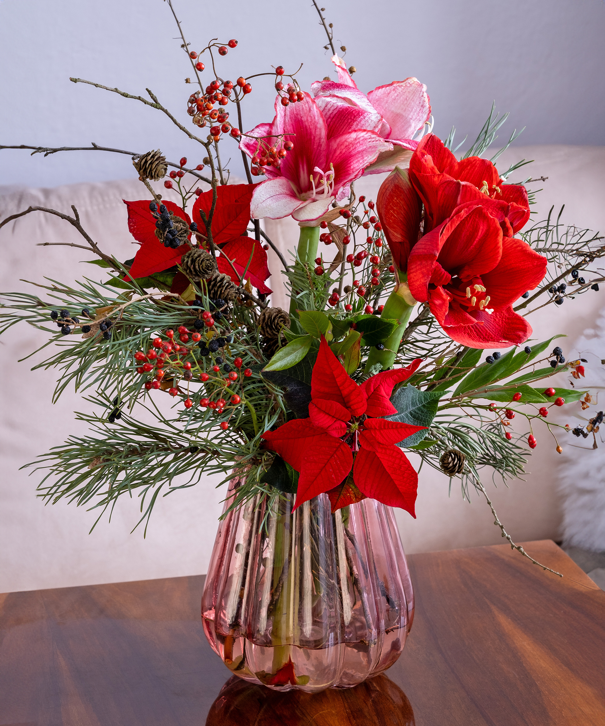 A winter bouquet of amaryllis, poinsettia, and coniferous branches in a fluted vase