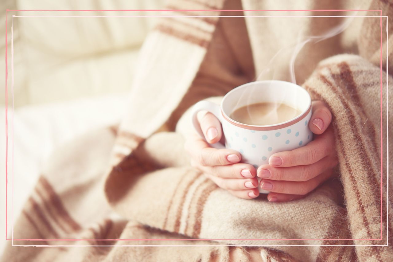 Woman warming hands on mug, wrapped in a blanket