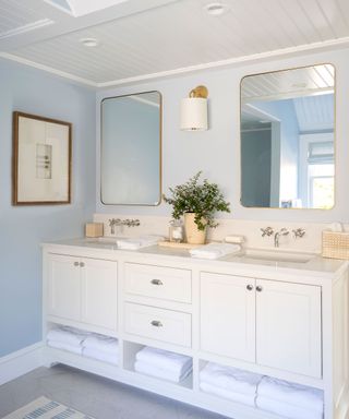 Blue and white bathroom with double vanity, matching mirrors, artwork on wall, decorative accessories on counter.