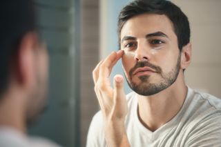 A man is looking in the mirror and applying face cream to his cheeks