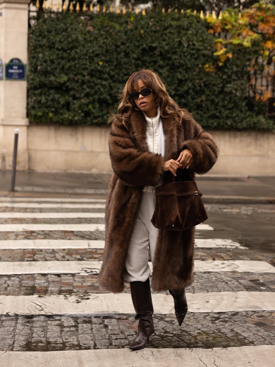 Ellie Delphine wears track pants tucked into knee-high boots with a faux fur coat.