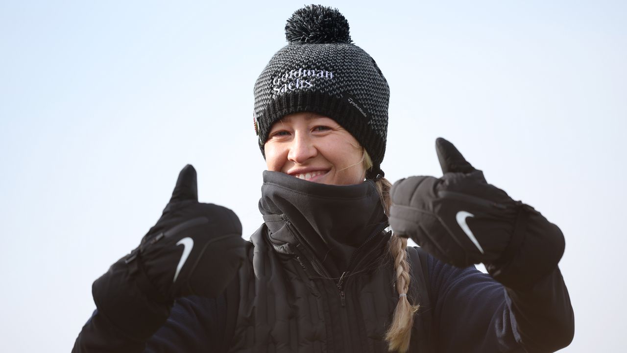 Nelly Korda smiles with her thumbs up whilst wearing a bobble hat and mittens