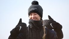 Nelly Korda smiles with her thumbs up whilst wearing a bobble hat and mittens