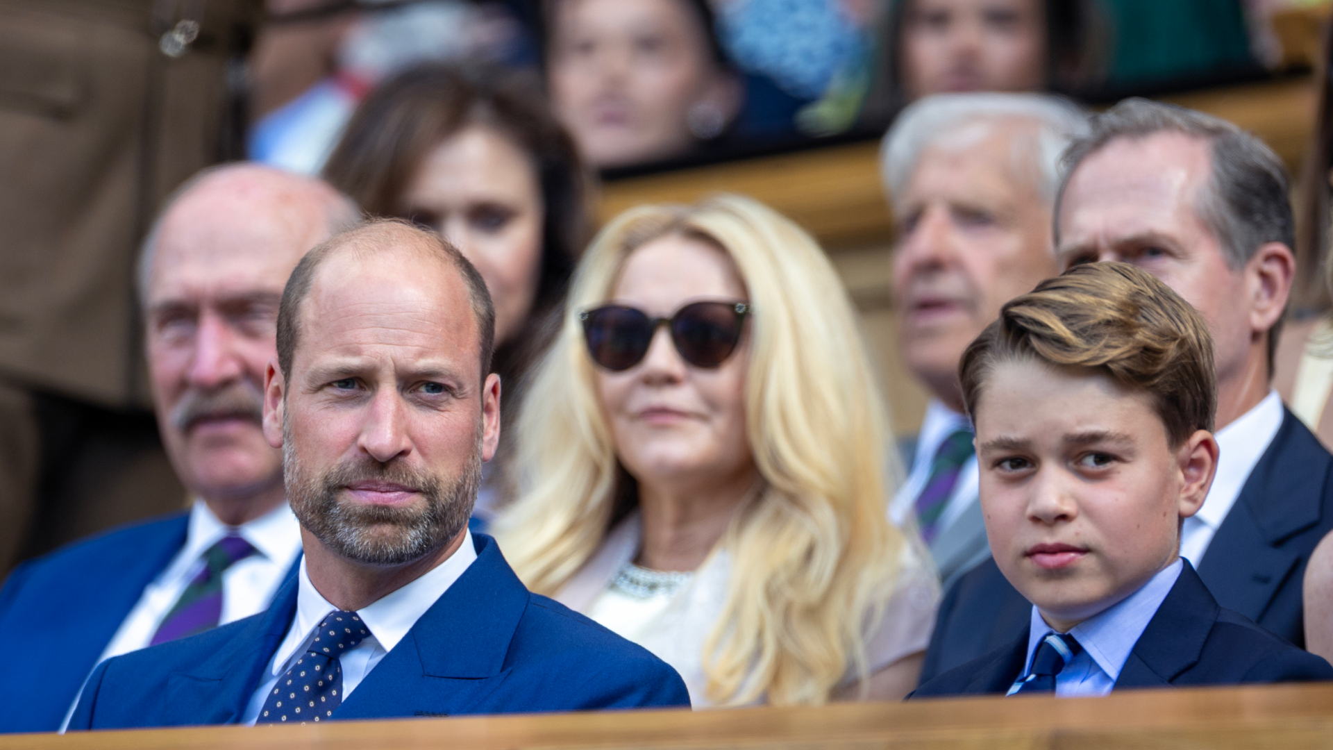 Prince George and Prince William sitting in the stands wearing blue suits at Wimbledon