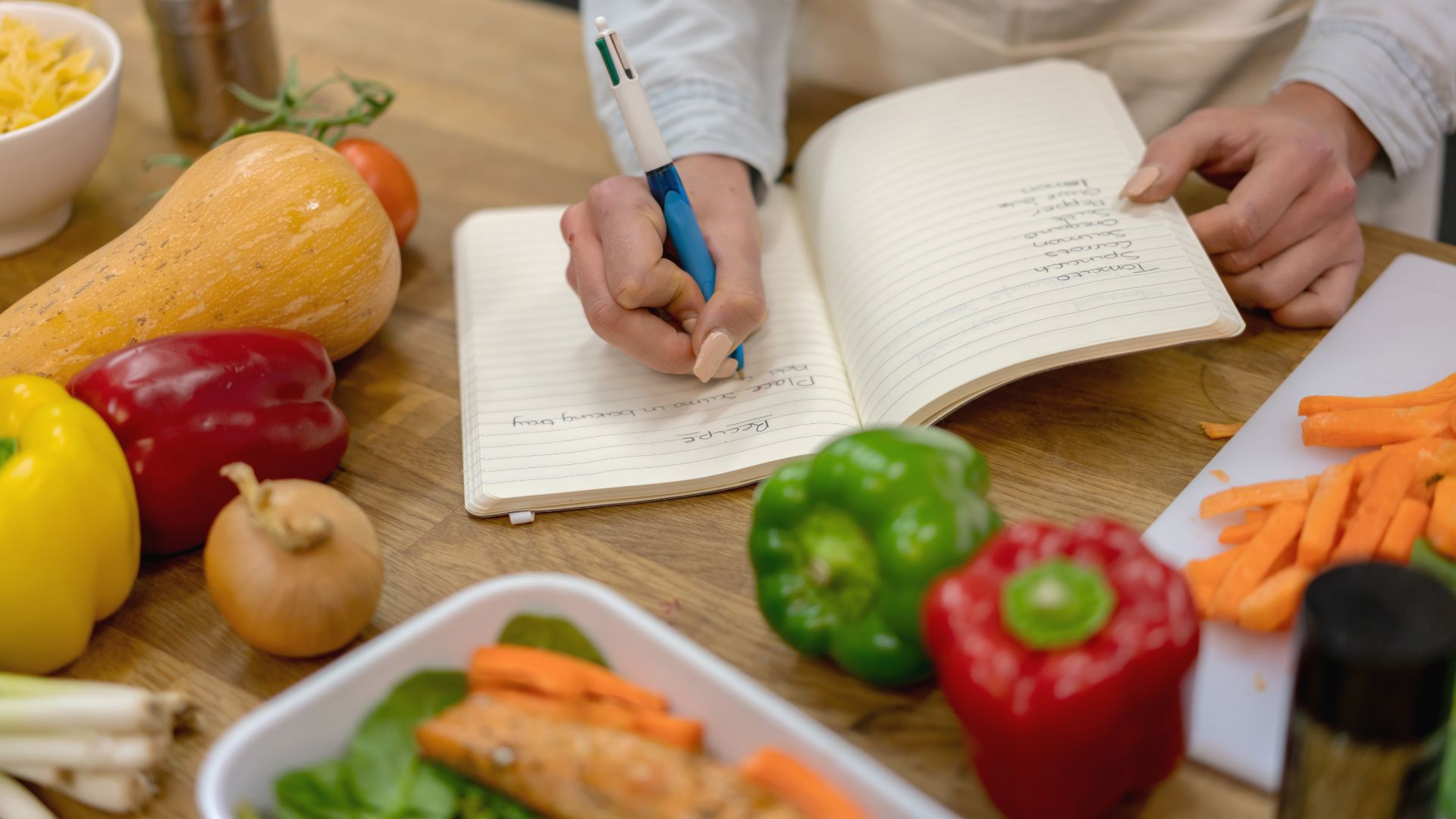 Person writing a shopping list next to fresh groceries