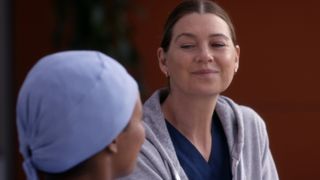 Ellen Pompeo as Meredith Grey smiling while sitting at the hospital in Grey's Anatomy season 19
