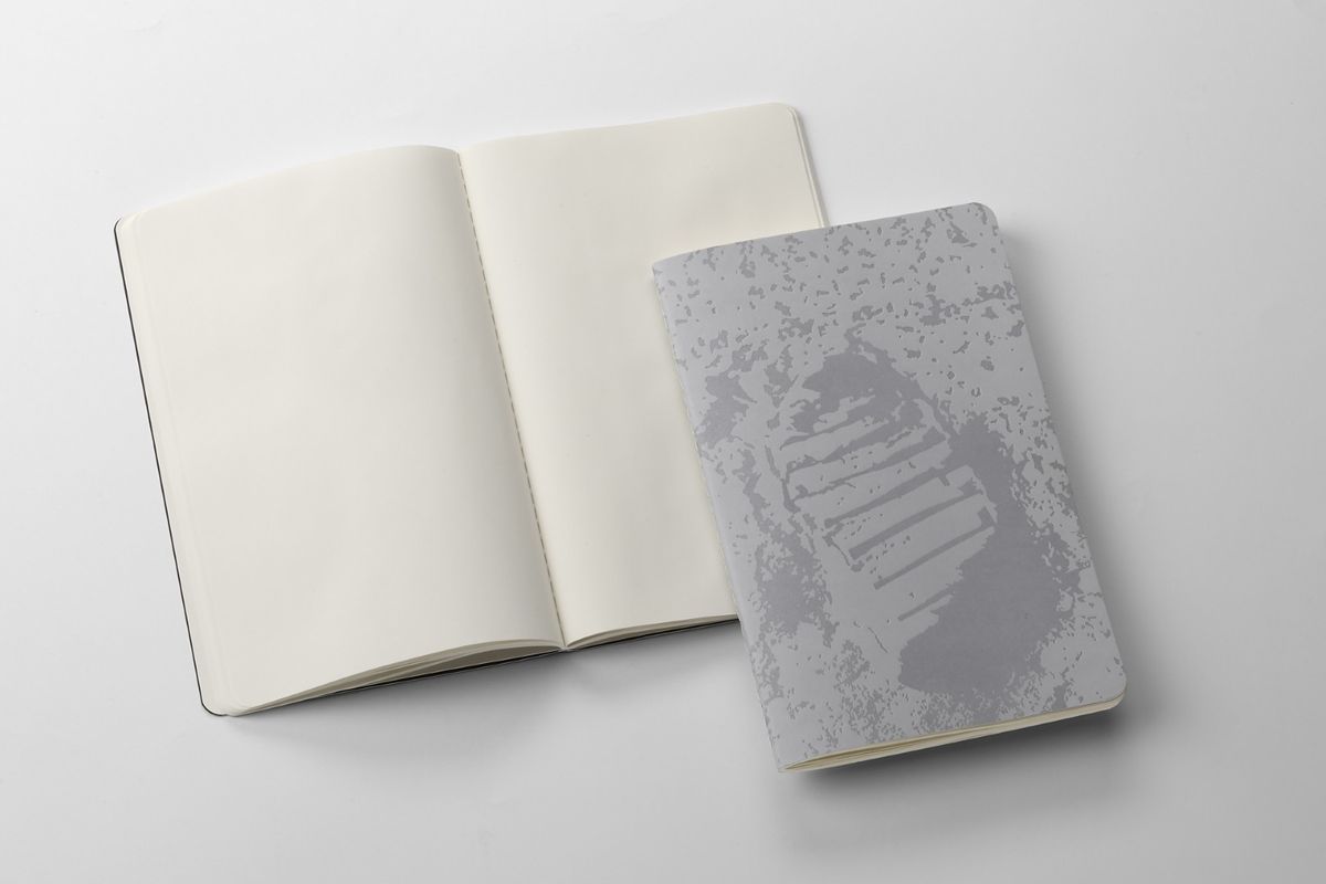 Two NASA-inspired Limited Edition Cahier Journals from Moleskine. Left: Open journal with blank pages. Right: Greyscale image of Neil Armstrong's moon footprint on the journal's cover.