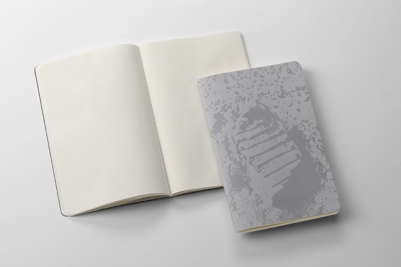 Two NASA-inspired Limited Edition Cahier Journals from Moleskine. Left: Open journal with blank pages. Right: Greyscale image of Neil Armstrong's moon footprint on the journal's cover.