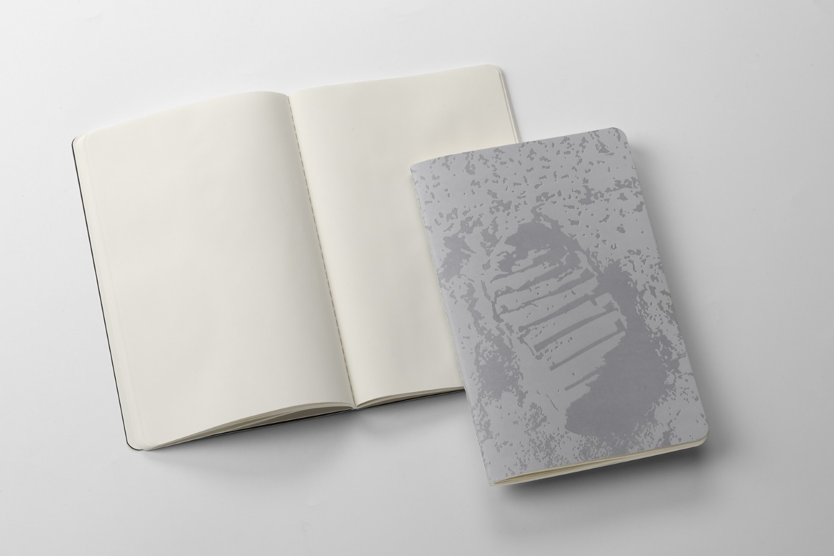 Two NASA-inspired Limited Edition Cahier Journals from Moleskine. Left: Open journal with blank pages. Right: Greyscale image of Neil Armstrong's moon footprint on the journal's cover.