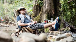 Man napping in a camping chair next to water stream during hiking