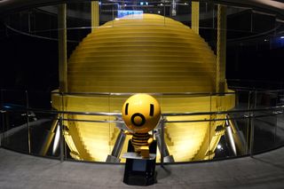 Large golden color orb suspends next to a viewing platform. A small damper "mascot" is located in front of it, it has a damper for a head and a yellow and black stripey body.