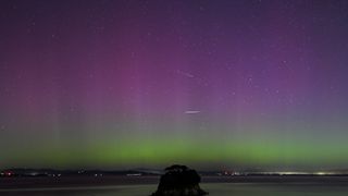 streaks of light cross the night sky, which is streaked with bands of purples and greens