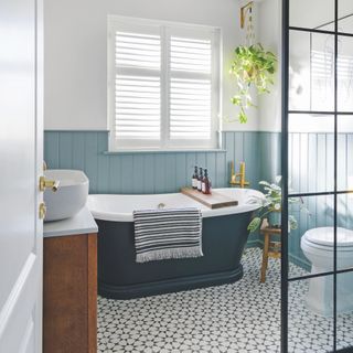 bathroom with navy roll top blue wall panelling and black adn white geometric tiles on floor