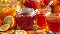 Jars of marmalade with slices of orange on wooden counter.