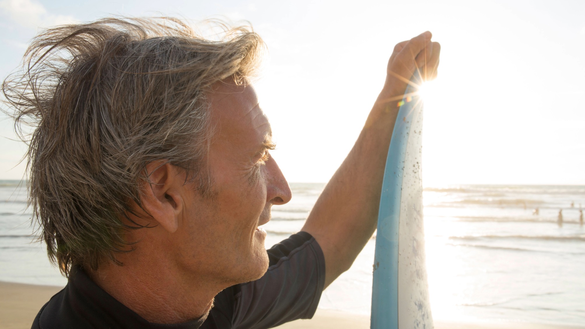 Mature man holds surfboard after surfing, looks off into the distance