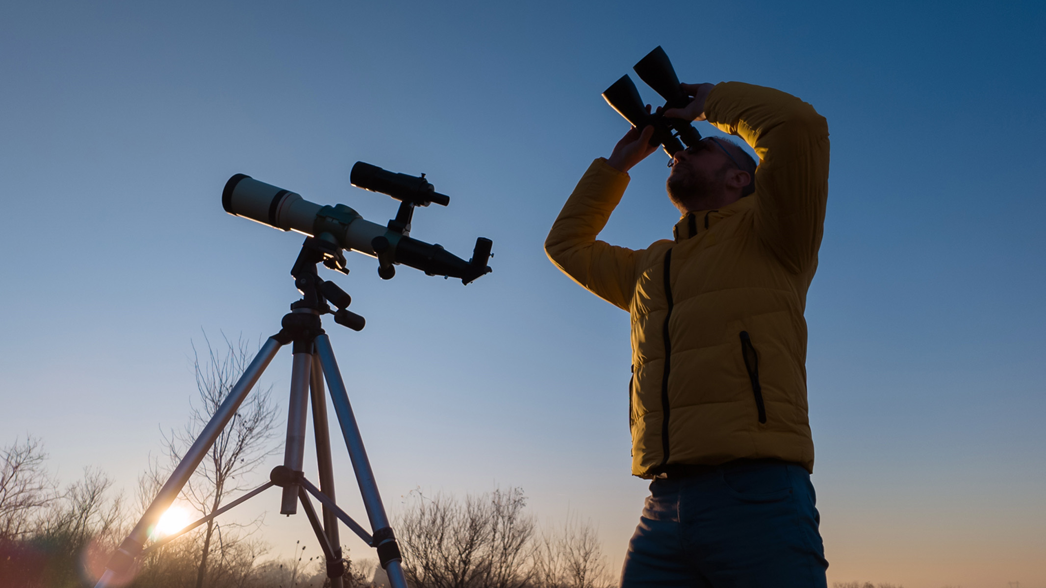 man using binoculars and a telescope at dusk