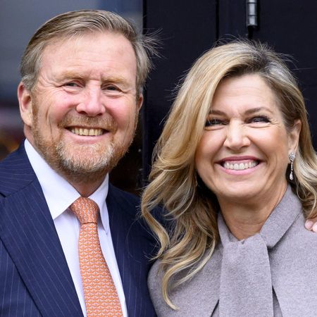 Queen Maxima wearing a gray coat and King Willem-Alexander wearing a blue suit and orange tie smiling 