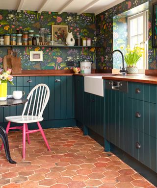 hexagonal terracotta floor tiles in a blue kitchen with patterned wallpaper and open shelving