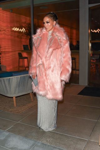 Jennifer Lopez looks pretty in pink as she steps out in a flirty, mid-length pink fur coat adorned with silver bows, layered over a white floor-length turtleneck gown, and finished off with heels and a chic bag, while leaving dinner in Beverly Hills after the GRAMMYs.