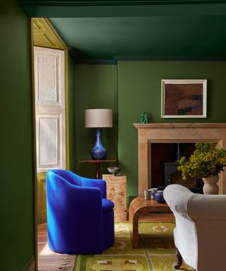 painted green living room with darker ceiling and a blue velvet armchair with a vintage rug