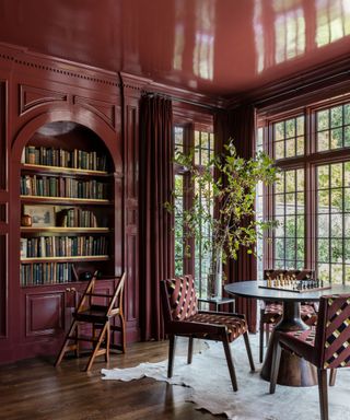 large dining room with dark red gloss color-drenched paint, built-in bookshelves with arch and red patterned dining chairs, large windows