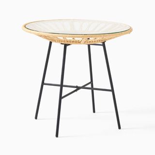 A round rattan bistro table with a glass top for sustainable furniture brands.