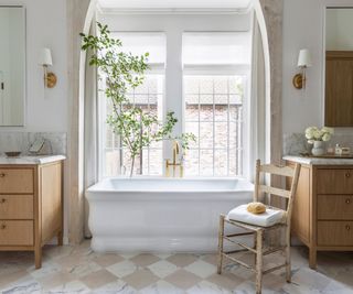 marble checkerboard bathroom floor with a large freestanding bathtub in the window and 2 wooden vanities