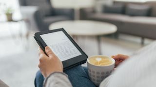 a person holding a Kindle eReader with a cup of coffee