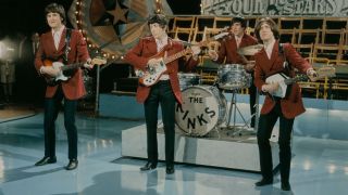 English rock group The Kinks, from left, Ray Davies, Pete Quaife, Mick Avory and Dave Davies (playing a Vox Phantom XII 12 string guitar) perform on the pop music television show Thank Your Lucky Stars for ABC Television at Alpha Television Studios in Birmingham, England in 1965. The band members are all wearing matching red jackets and pink shirts.