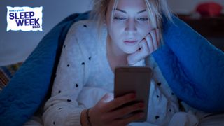 Woman laying on her front in bed looking at her phone