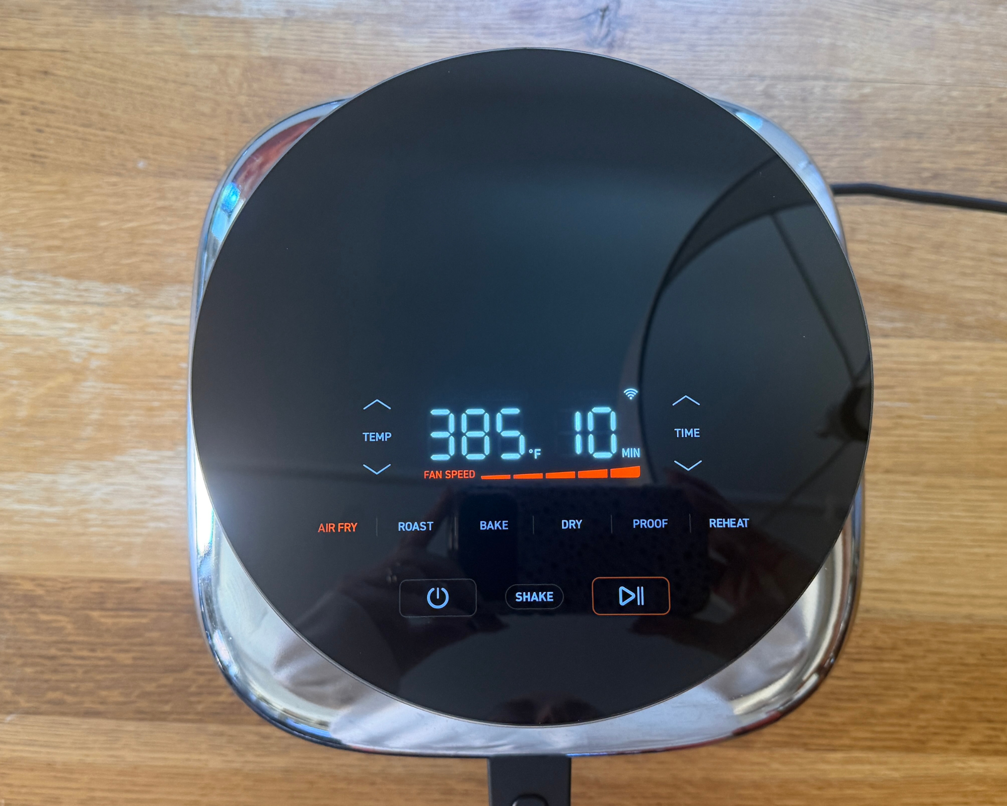 Cosori Iconic air fryer with display facing up, sitting on a brown, wooden table