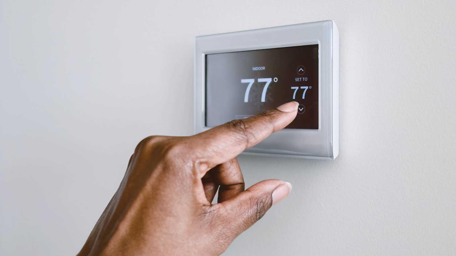 Hand pressing smart thermostat on white wall