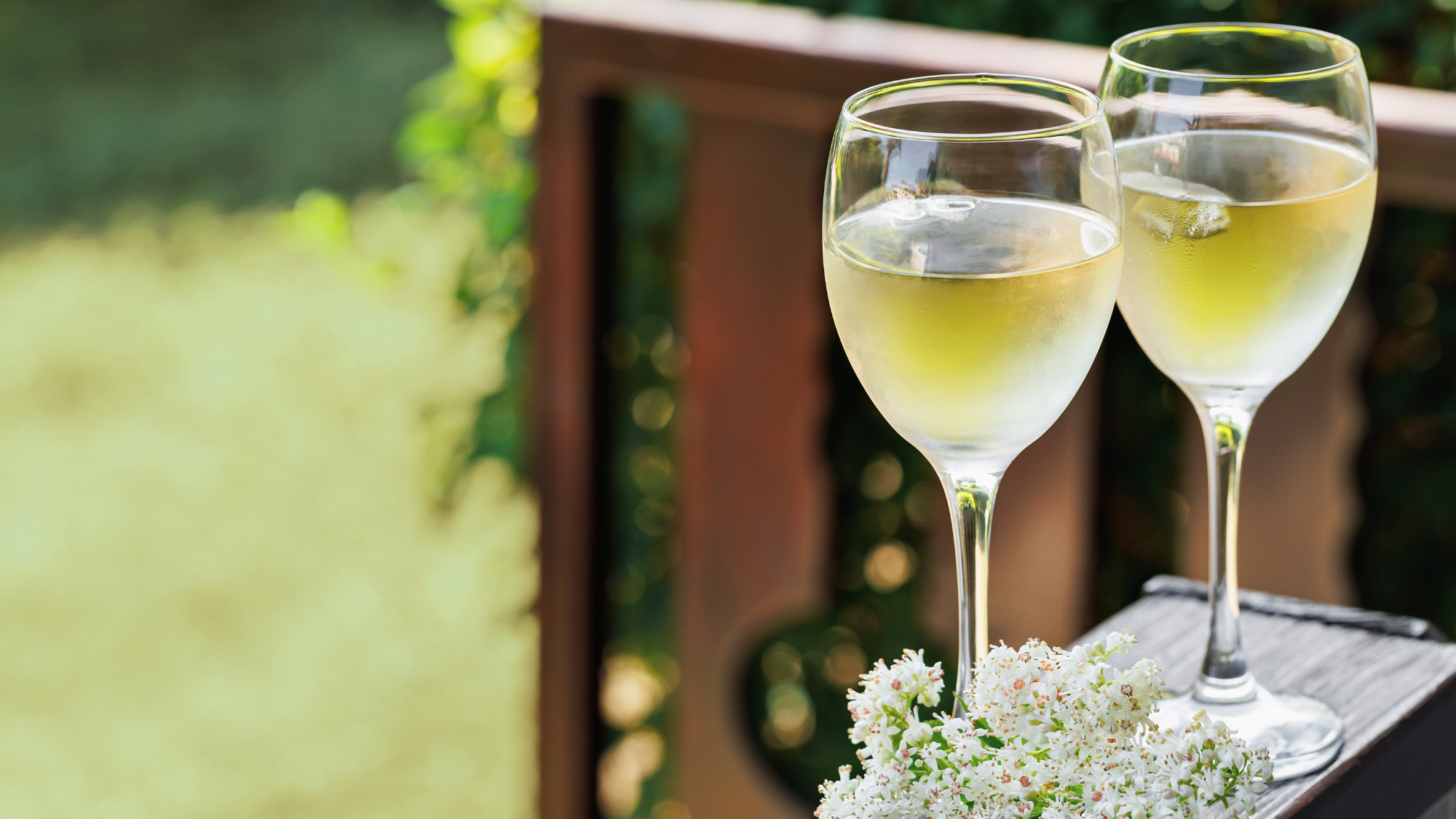 A couple glasses of wine placed on an outdoor ledge with greenery in the background
