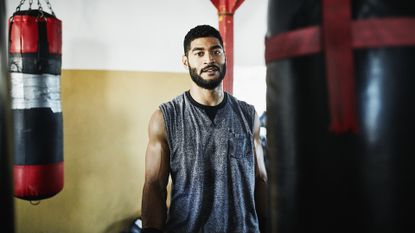 Get fit 2024: Portrait of male boxer standing by heavy bag in boxing gym