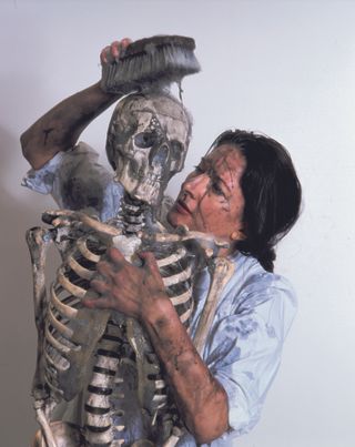 Marina Abramovic is holding a skeleton and washing it. There is dirt on her and the skeleton.